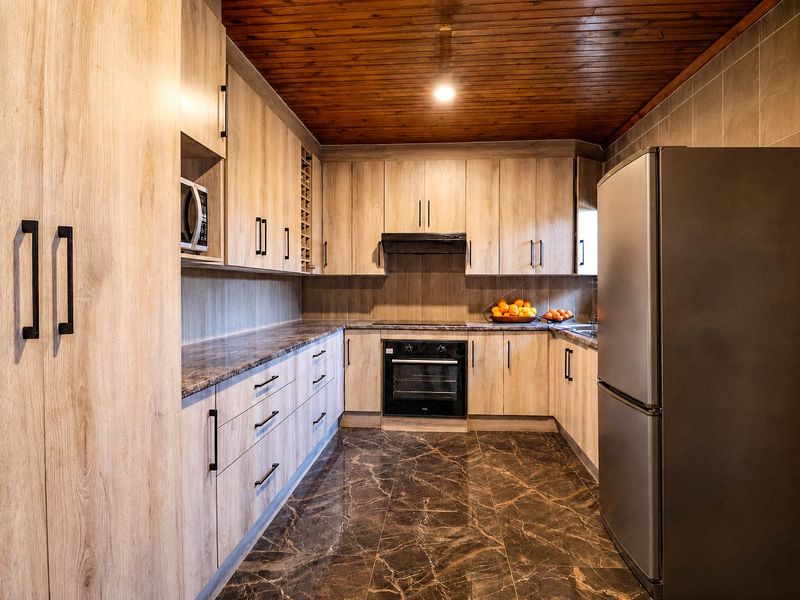 A well-maintained kitchen featuring light wood-grain cabinetry, dark marble-effect tiled flooring, a timber-paneled ceiling, and integrated appliances including an oven and hob.