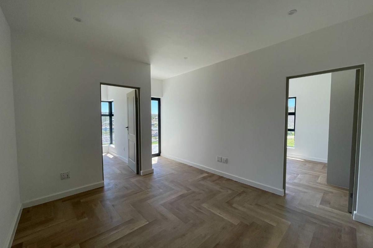 A bright, empty room featuring high-quality herringbone timber flooring, recessed ceiling lighting, and multiple doorways leading to adjacent spaces with large windows.