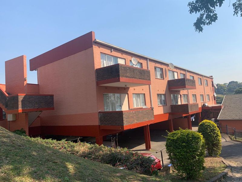 Rear view of a multi-story apartment building featuring brick facade, private balconies, and a covered ground-level parking area.