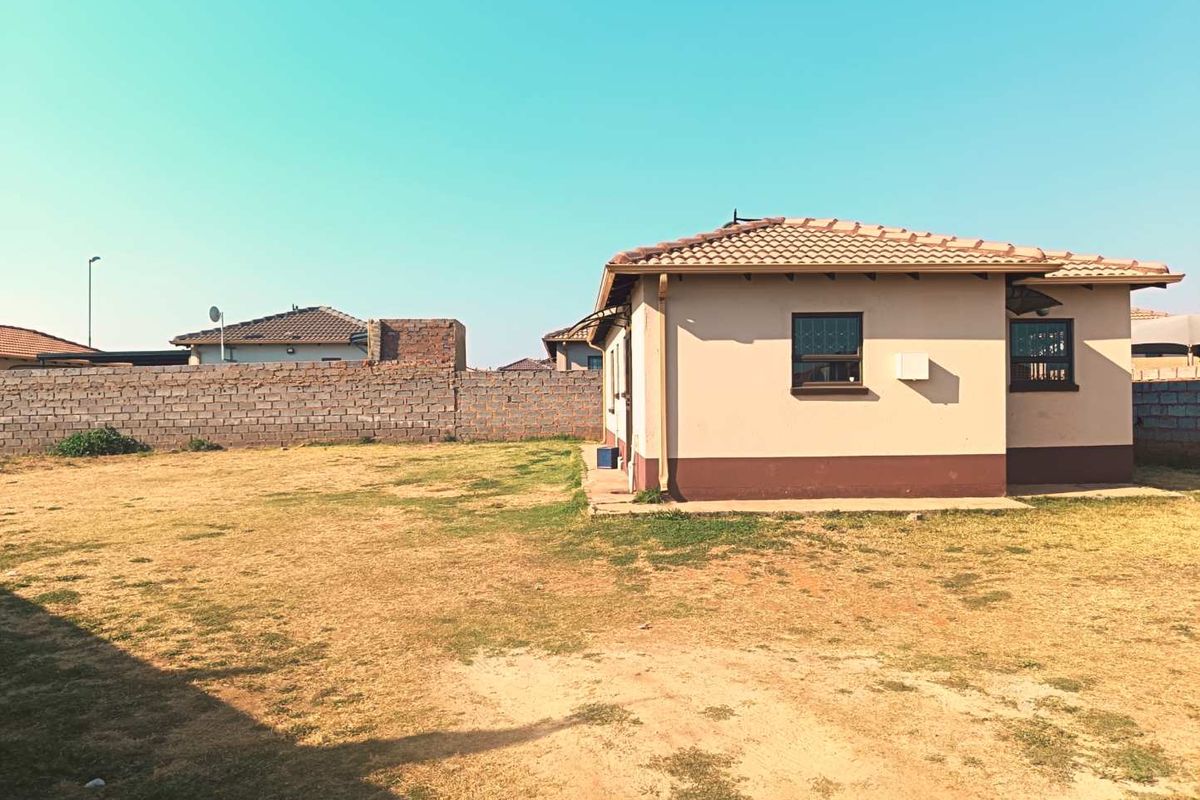 Rear view of the property featuring a large open yard, concrete tiled roof, and perimeter brick walling.