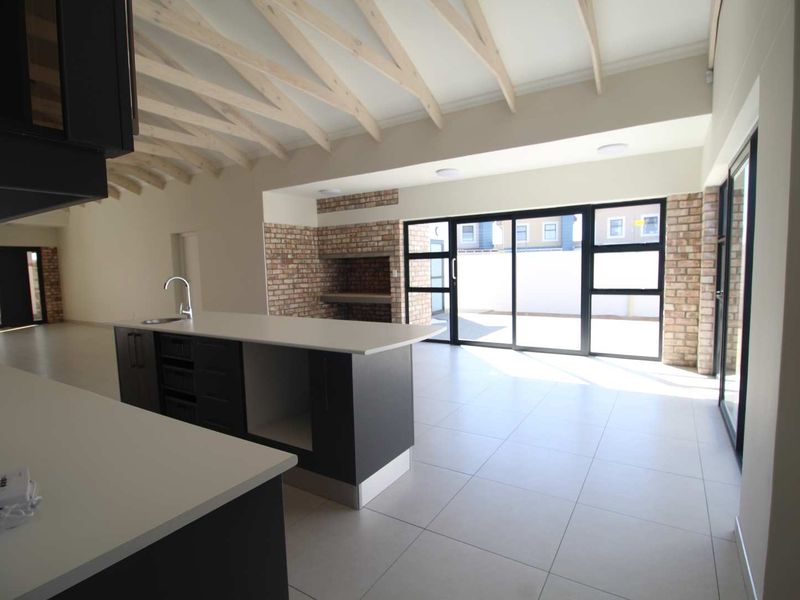 Spacious open-plan living area featuring a modern kitchen island, exposed timber rafters, and a built-in brick fireplace with seamless access to the outdoor patio.