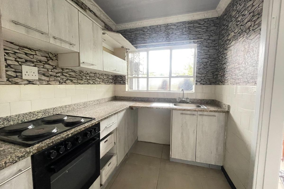 A compact kitchen featuring built-in cabinetry, granite countertops, a stainless steel sink, and an electric stove, requiring some cosmetic updates.
