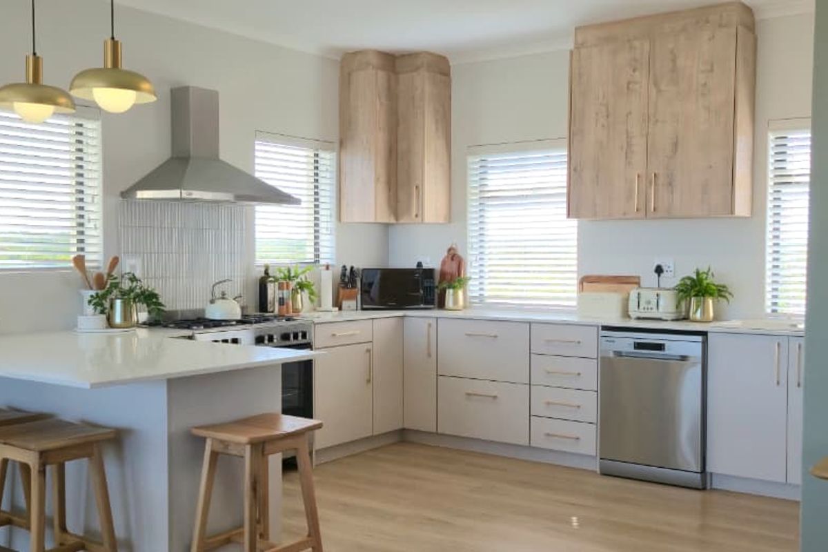 Modern kitchen featuring light wood cabinetry, stone countertops, stainless steel appliances, a breakfast bar, and a tiled backsplash.