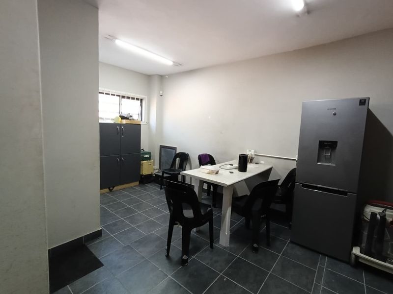 A functional utility or break room space featuring tiled flooring, fluorescent lighting, and a window with security bars.