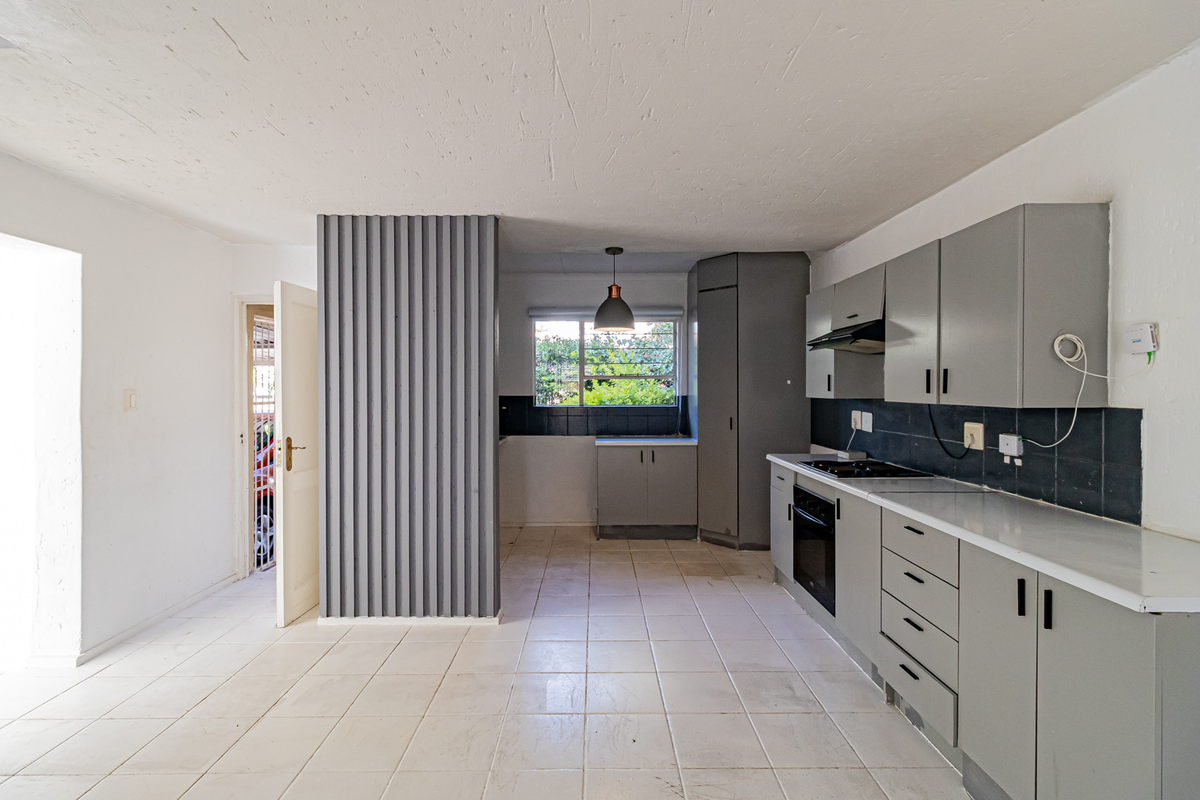 A functional, empty kitchen featuring grey built-in cabinetry, tiled flooring, and integrated appliances, offering a blank canvas for modern renovation.