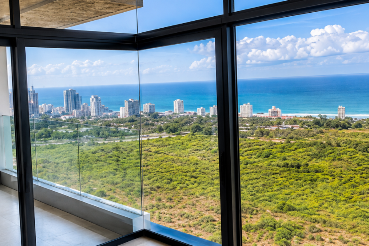 Modern living area featuring expansive floor-to-ceiling windows with panoramic ocean and coastal views, complemented by sleek tiled flooring and a glass balcony balustrade.
