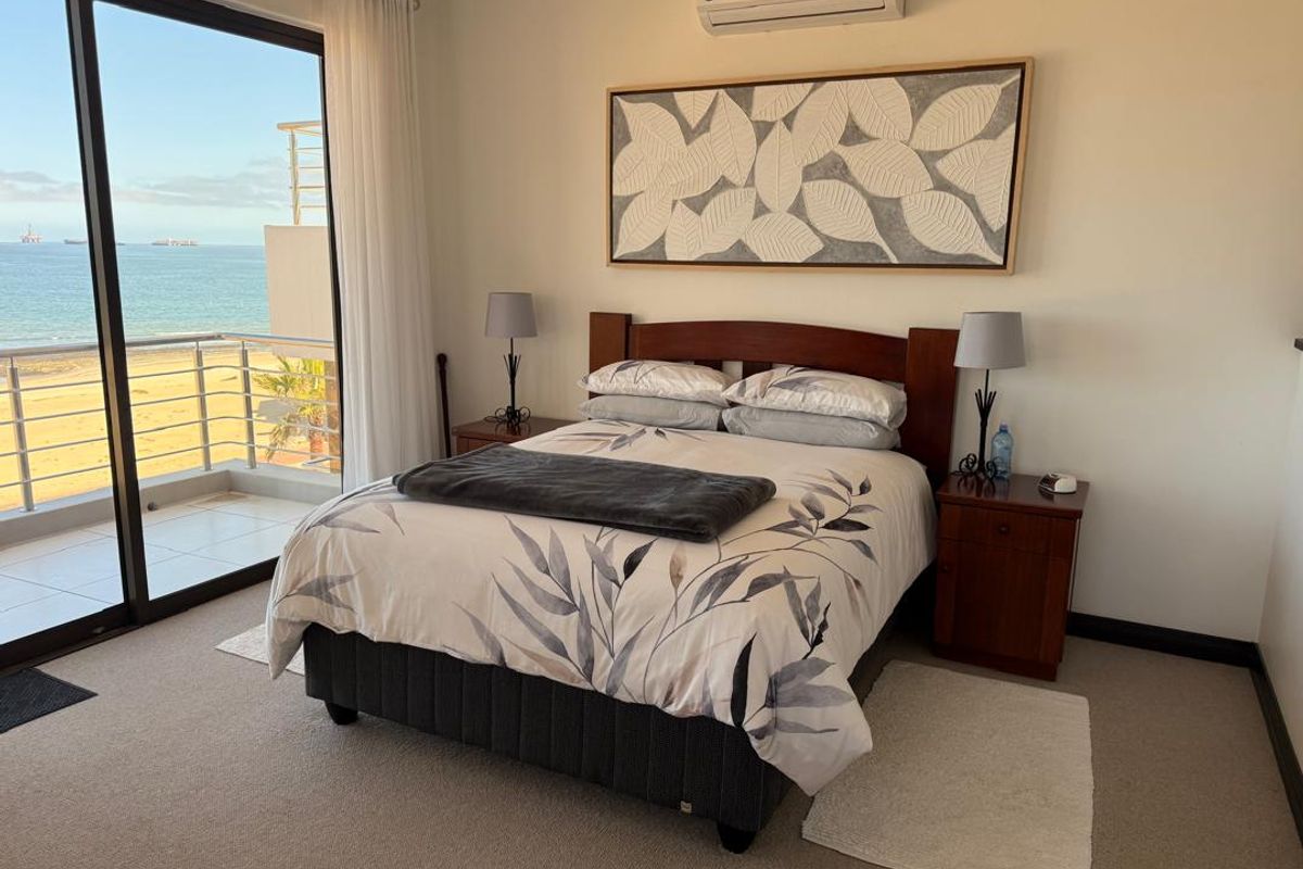 A well-maintained bedroom featuring carpet flooring, a wall-mounted air conditioner, and large sliding glass doors opening onto a balcony with ocean views.
