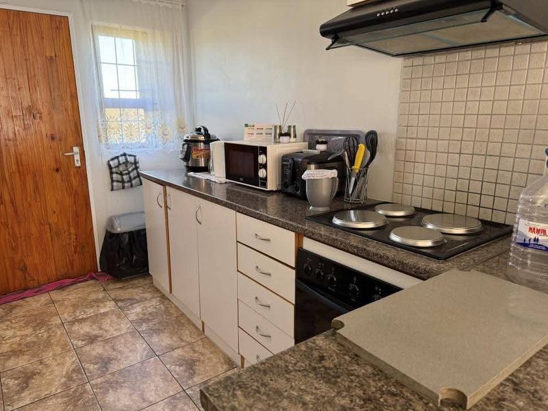 Functional kitchen featuring laminate cabinetry, electric hob with extractor fan, tiled backsplash, and durable floor tiles.