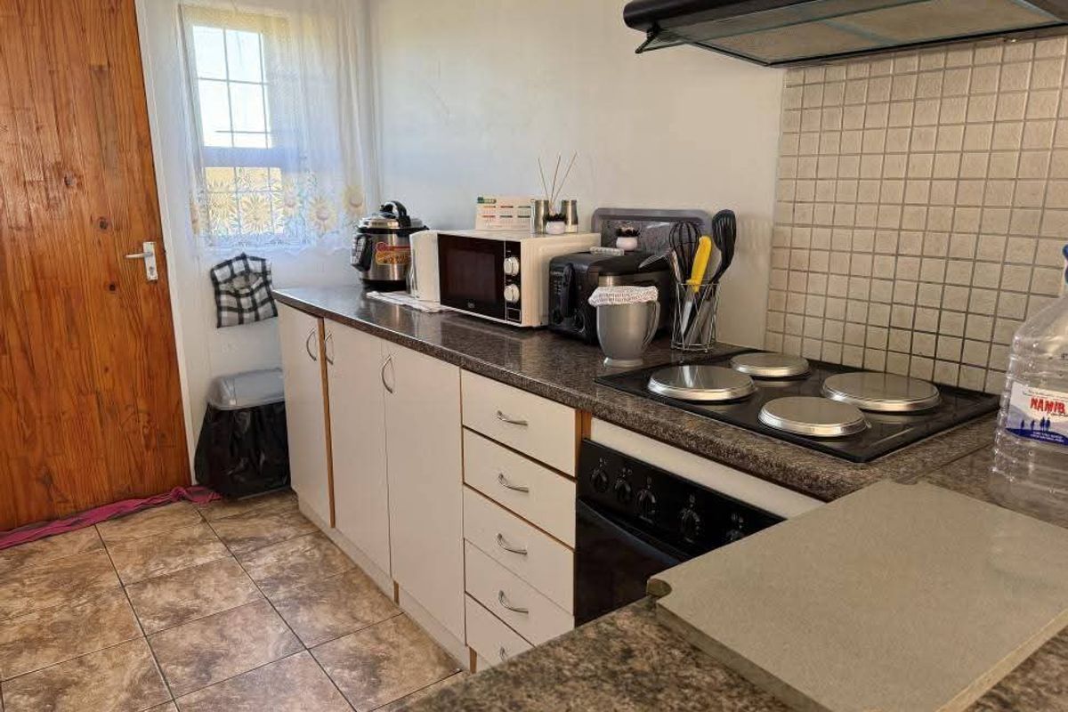 Functional kitchen featuring laminate cabinetry, electric hob with extractor fan, tiled backsplash, and durable floor tiles.