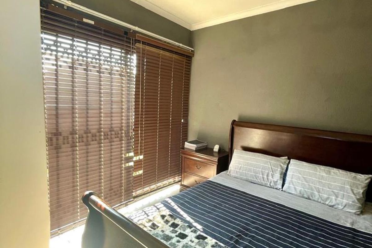 A bedroom featuring tiled flooring, a ceiling fan, and built-in cupboards, with natural light entering through venetian blinds.