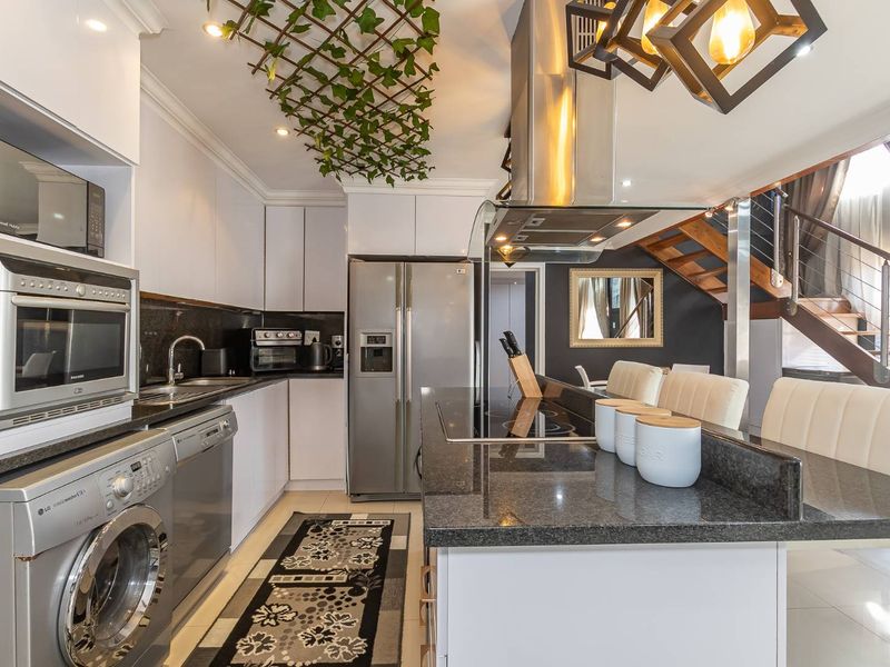 Modern open-plan kitchen featuring granite countertops, built-in appliances, and a sleek breakfast bar, seamlessly connected to the living area and staircase.