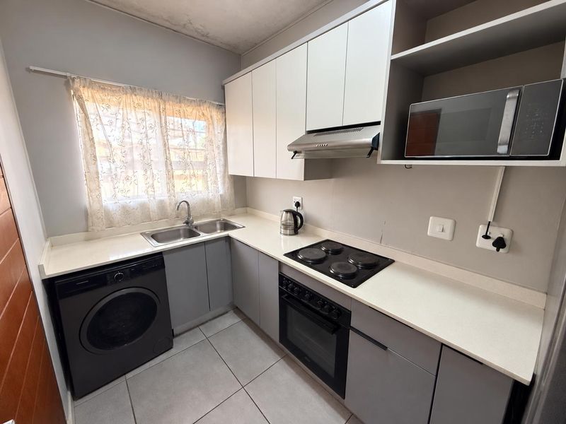 Compact kitchen featuring modern grey and white cabinetry, integrated appliances, tiled flooring, and a double sink with a window view.