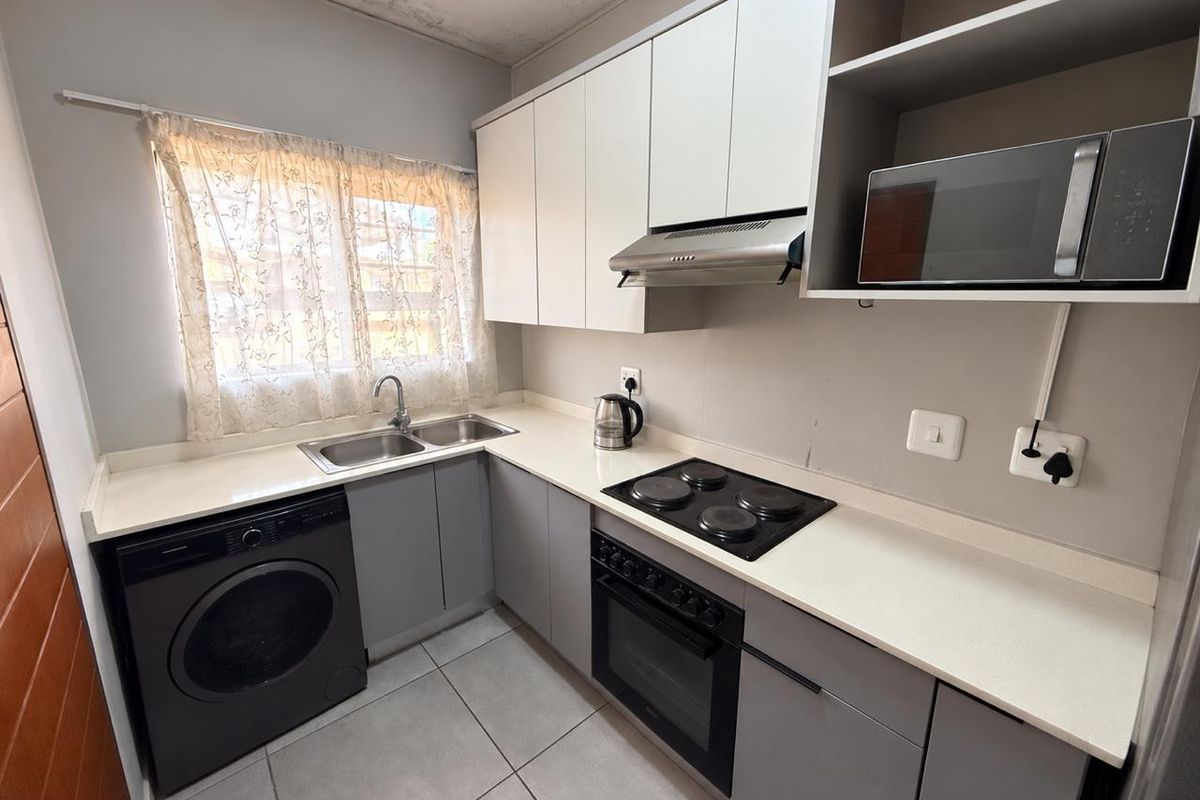 Compact kitchen featuring modern grey and white cabinetry, integrated appliances, tiled flooring, and a double sink with a window view.