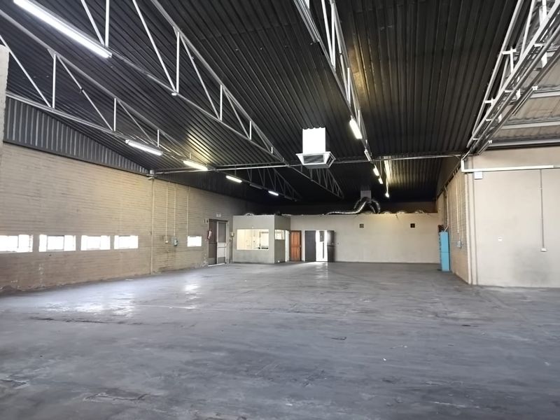 Spacious industrial utility space featuring high exposed steel roof trusses, concrete flooring, and an integrated internal office partition.