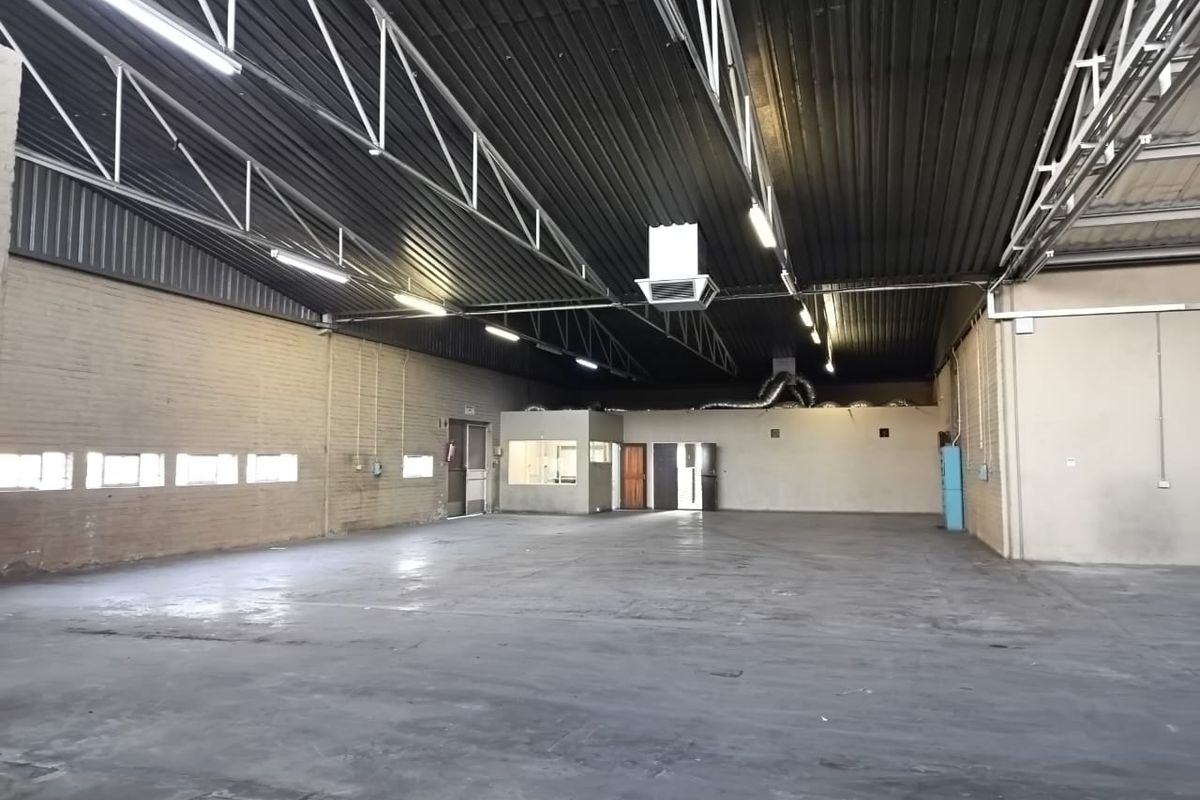 Spacious industrial utility space featuring high exposed steel roof trusses, concrete flooring, and an integrated internal office partition.
