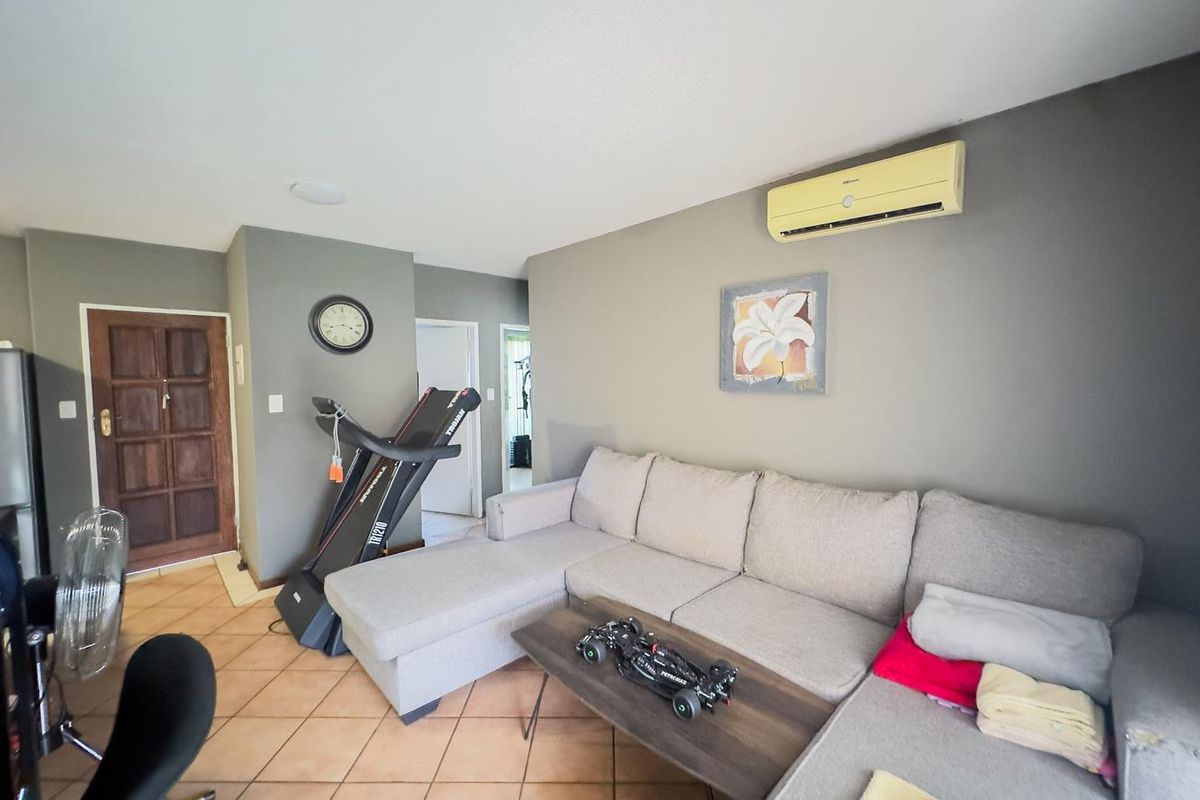 A living room featuring tiled flooring, a wall-mounted split-system air conditioner, and access to the main entrance.