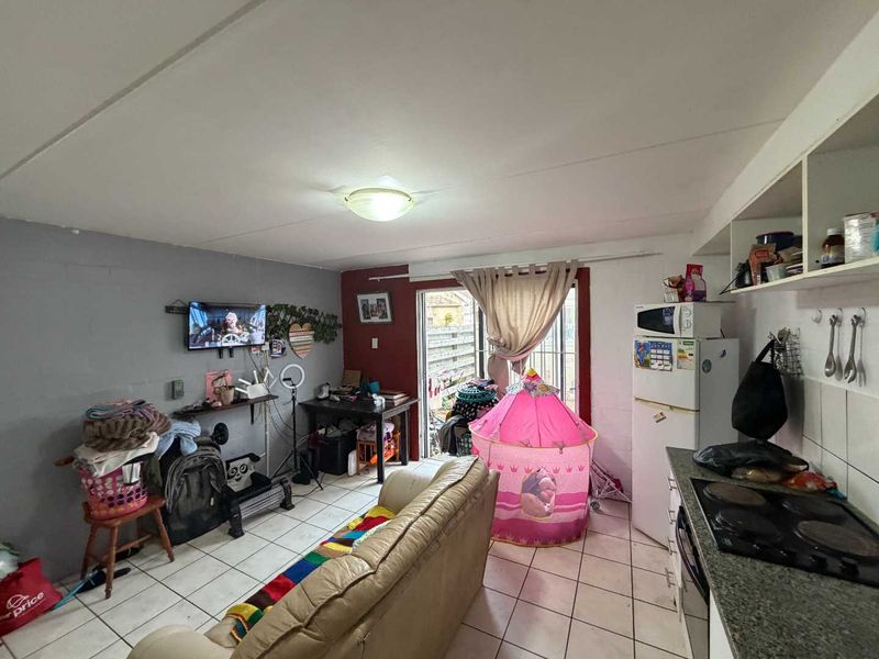 Open-plan living and kitchen area featuring tiled flooring, built-in cabinetry with granite countertops, and direct access to an outdoor space via sliding glass doors.