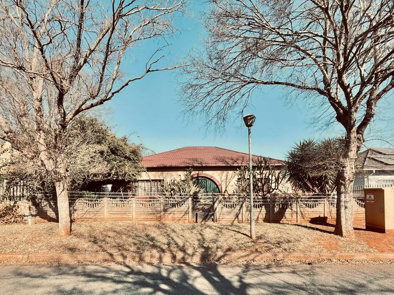 Front view of a single-story house featuring a tiled roof, arched entrance, and a precast concrete boundary wall with mature trees.