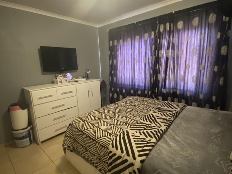 A bedroom featuring tiled flooring and neutral wall finishes, providing a functional space with standard lighting and window treatments.