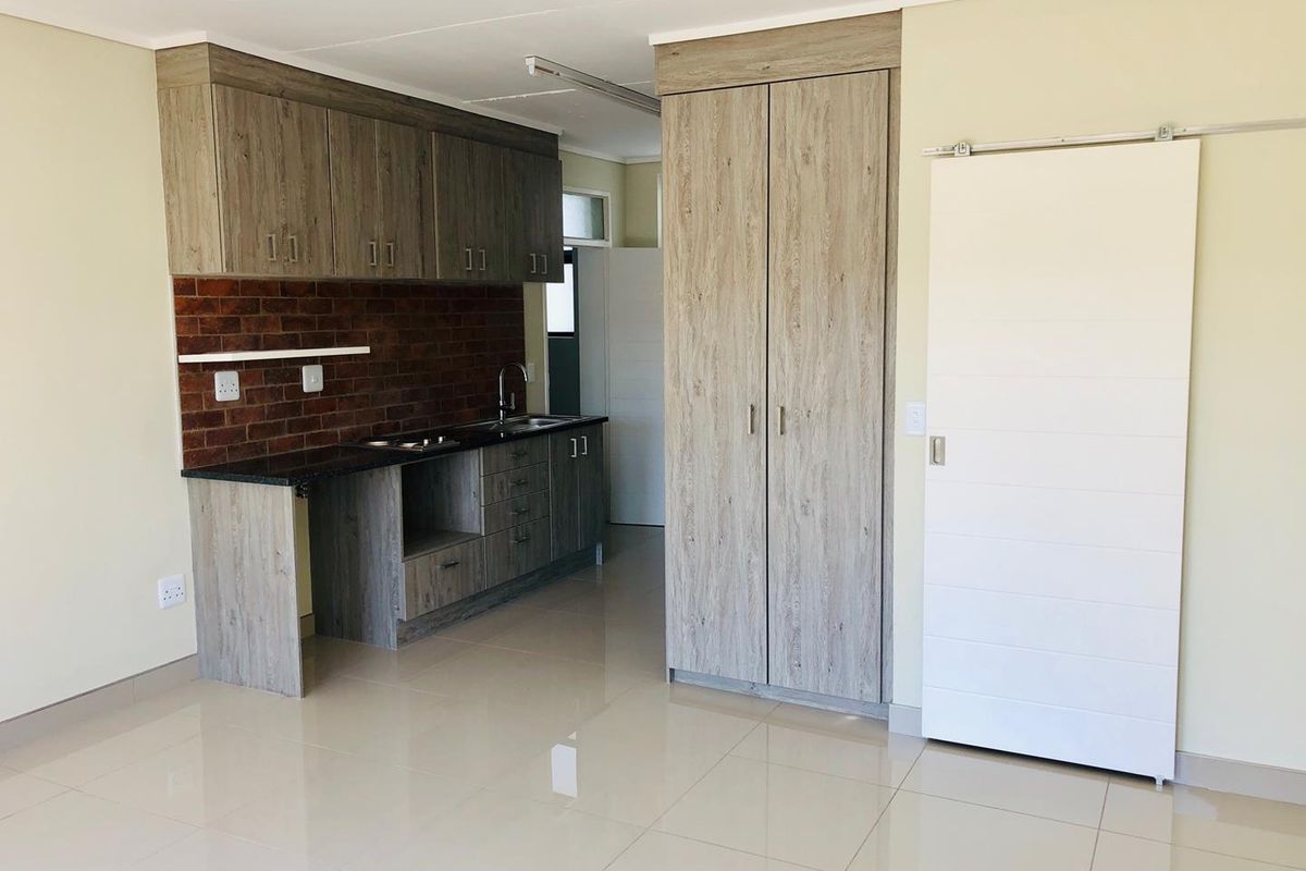Modern kitchenette featuring wood-look cabinetry, a brick-style backsplash, dark countertops, and a built-in cupboard, complemented by polished floor tiles and a sliding door.