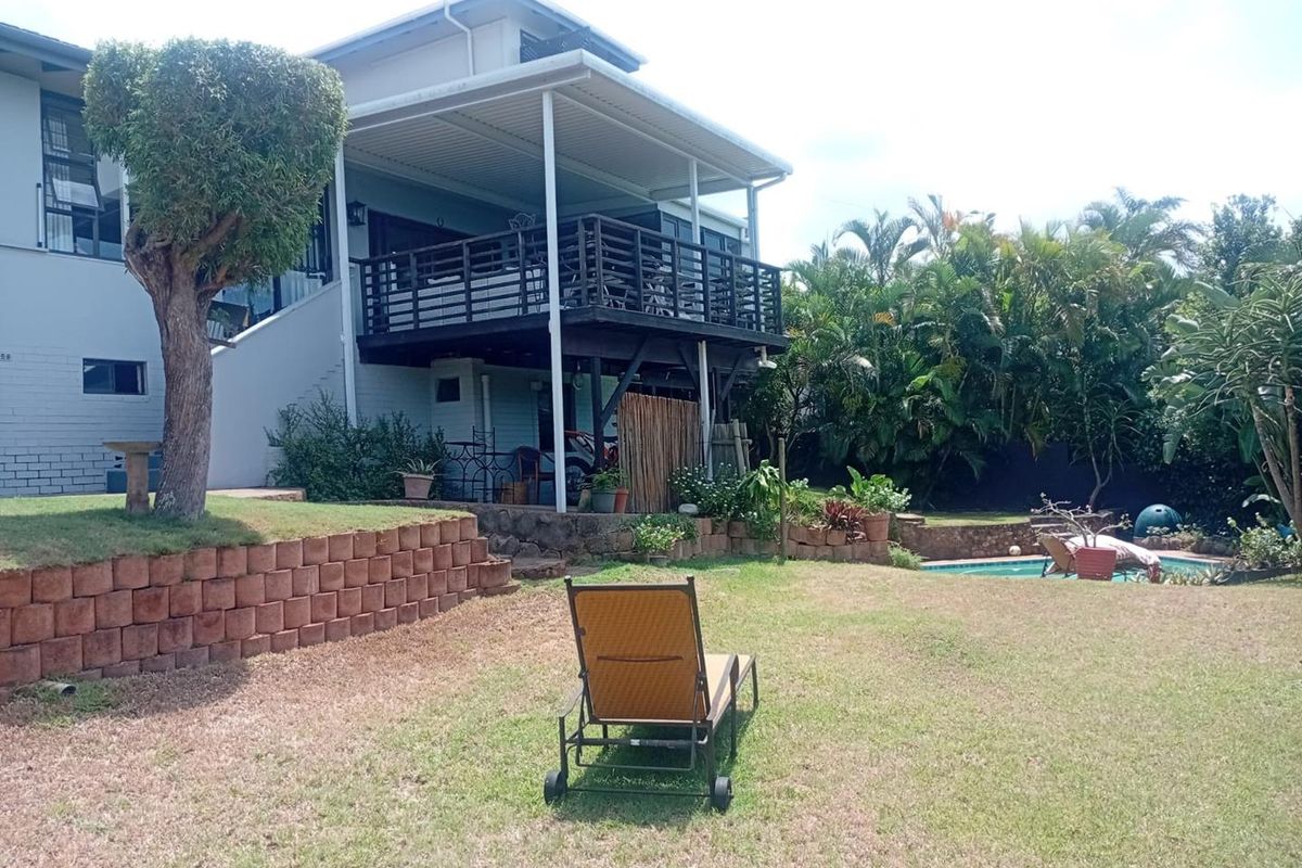 Rear view of the property featuring an elevated timber balcony, a landscaped garden with retaining walls, and a swimming pool.