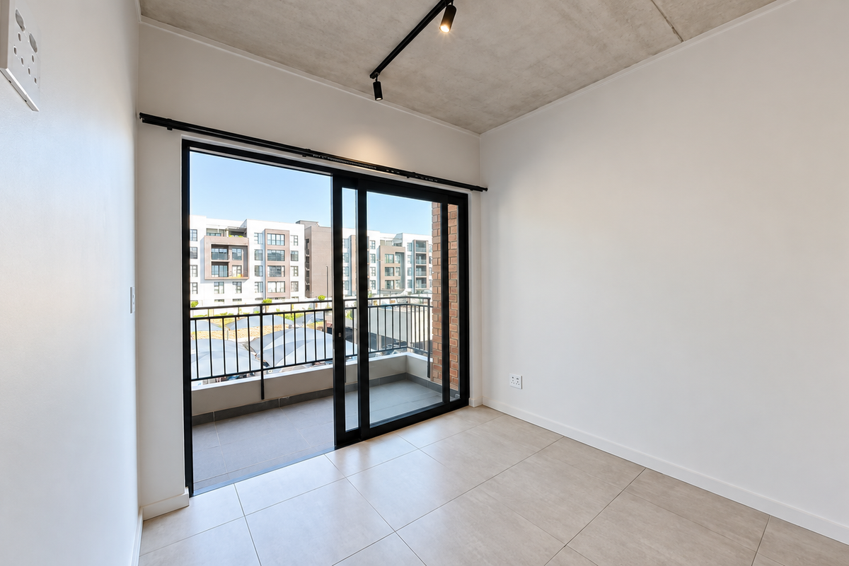 A bright, modern bedroom featuring an exposed concrete ceiling, sleek track lighting, tiled floors, and a sliding glass door leading to a private balcony.