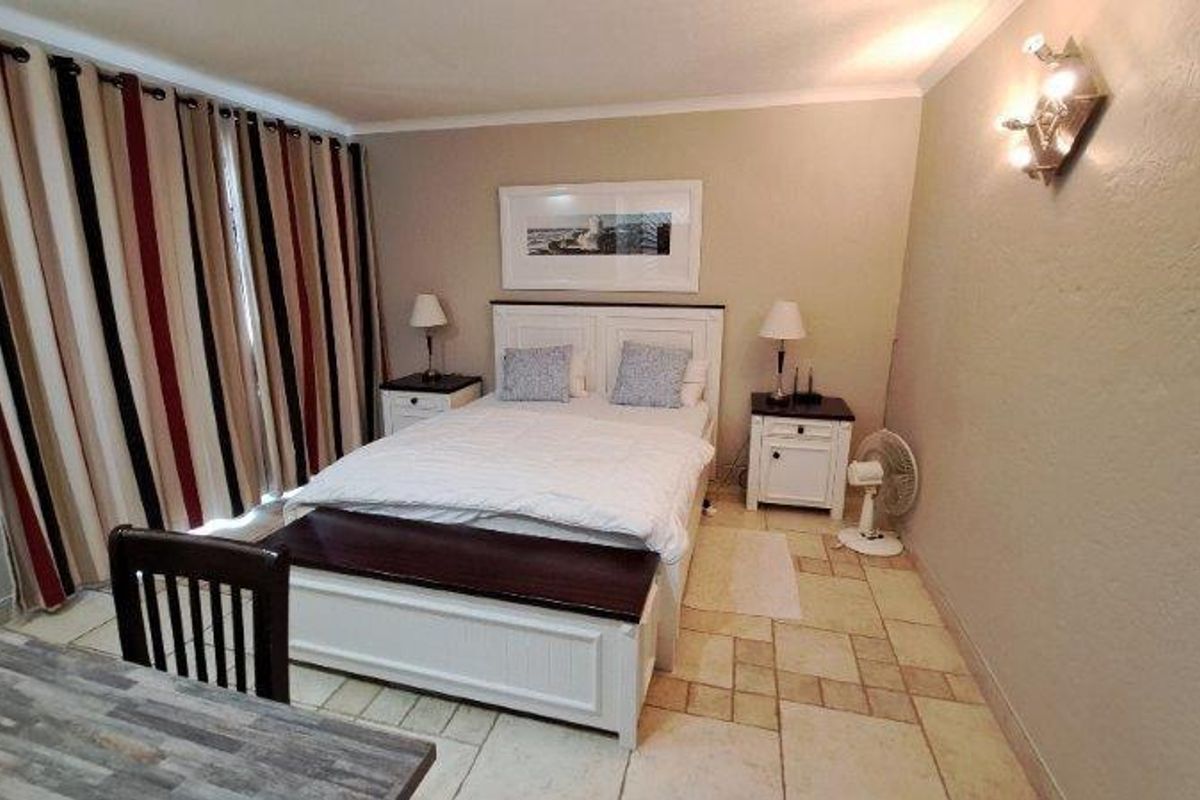 A bedroom featuring tiled flooring, a wall-mounted light fixture, and large sliding glass doors covered by floor-to-ceiling curtains.