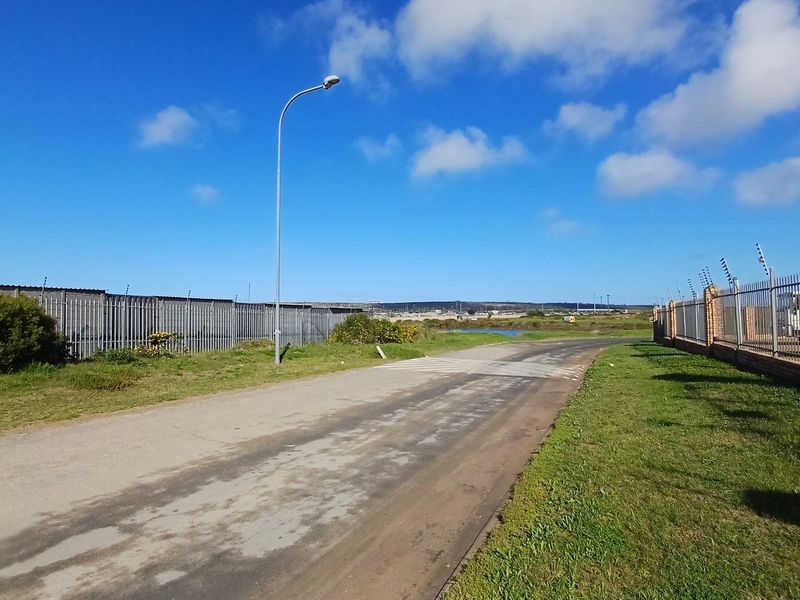 Street view showing the access road to the industrial property, featuring perimeter brick walling and electric fencing.