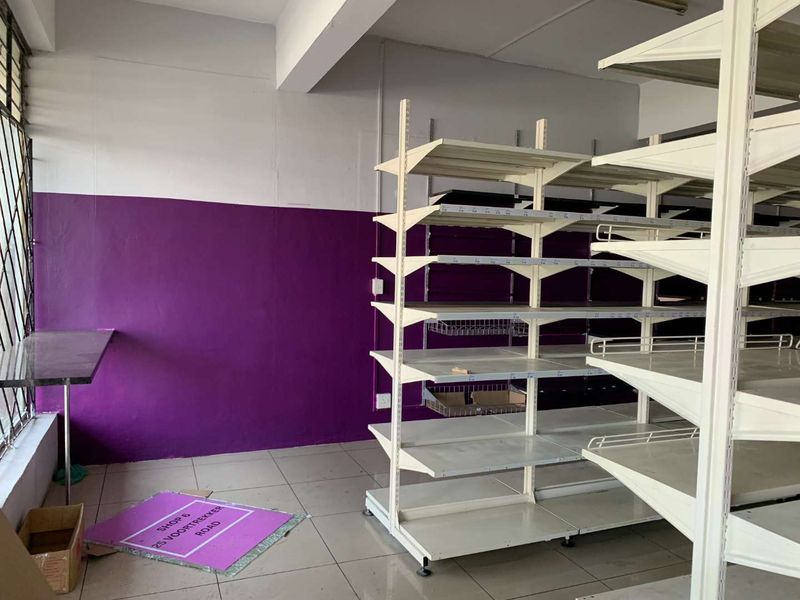 Empty retail space featuring tiled flooring, metal shelving units, and security bars on windows, suitable for various commercial business applications.