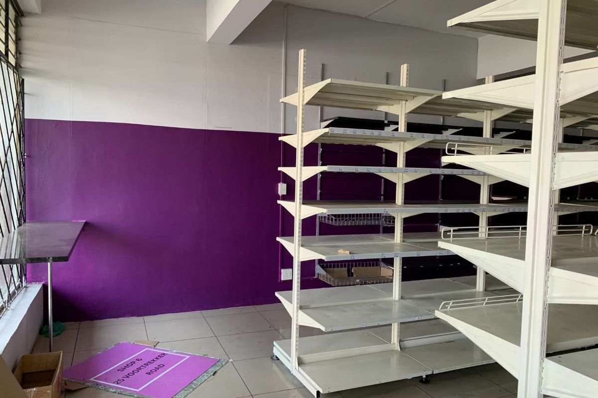 Empty retail space featuring tiled flooring, metal shelving units, and security bars on windows, suitable for various commercial business applications.