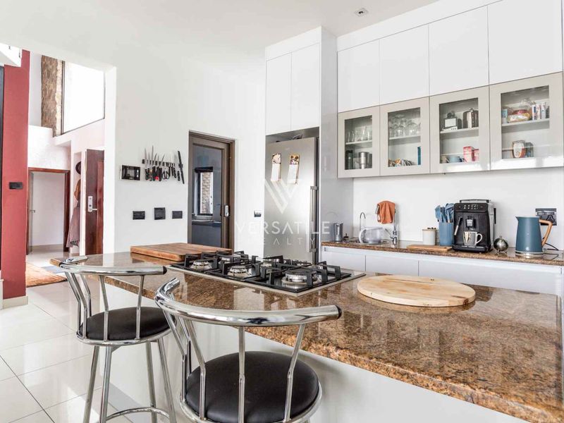 Modern kitchen featuring granite countertops, a gas hob, ample built-in cabinetry, and glass-fronted wall units, finished with clean tiled flooring.