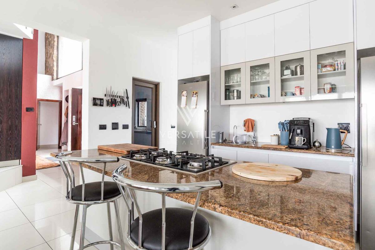 Modern kitchen featuring granite countertops, a gas hob, ample built-in cabinetry, and glass-fronted wall units, finished with clean tiled flooring.