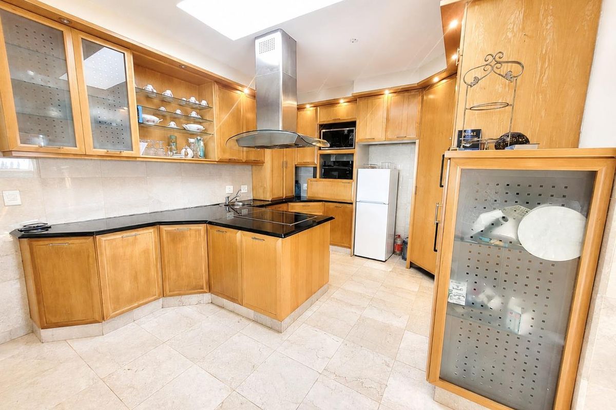 Spacious kitchen featuring extensive wooden cabinetry, black granite countertops, integrated appliances, and a large skylight providing ample natural light.