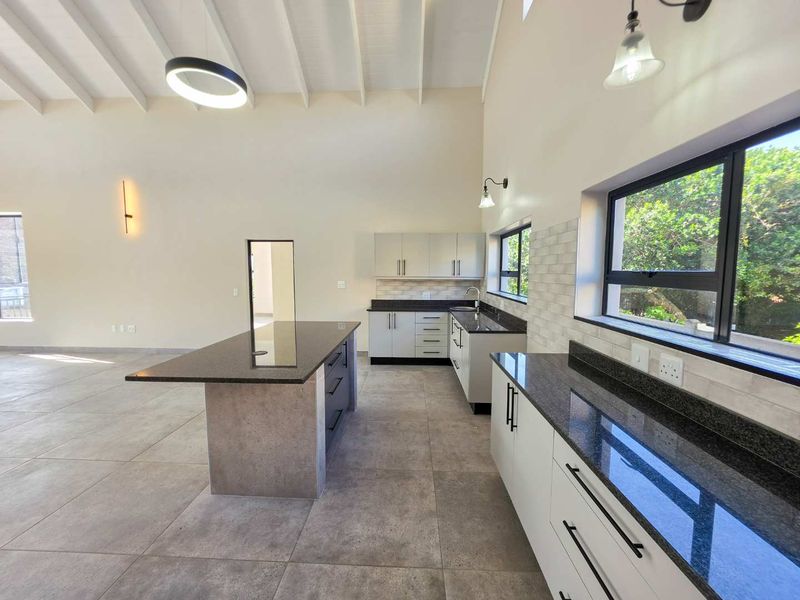 Modern, spacious kitchen featuring a large island, granite countertops, sleek cabinetry, and high vaulted ceilings with exposed beams, offering a bright and open layout.