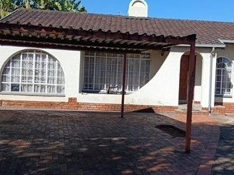 Front elevation of a single-story apartment building featuring a tiled roof, arched windows, and a paved driveway with an attached carport.