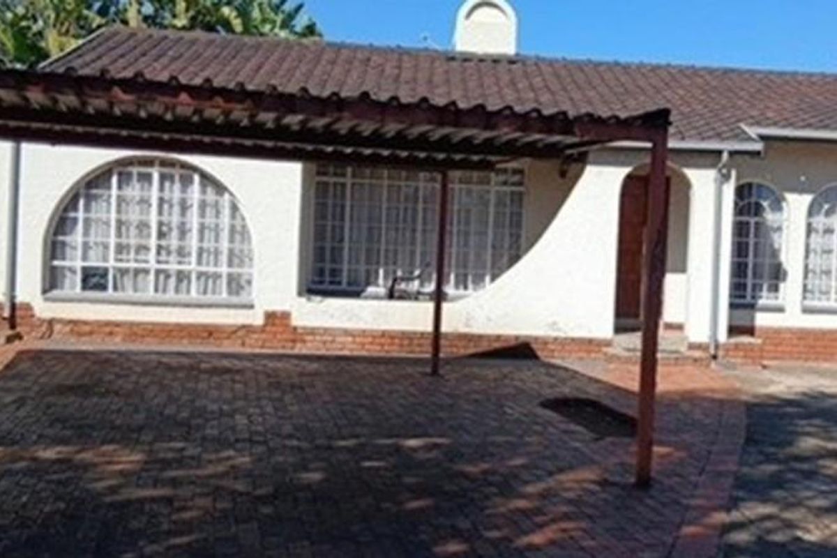 Front elevation of a single-story apartment building featuring a tiled roof, arched windows, and a paved driveway with an attached carport.