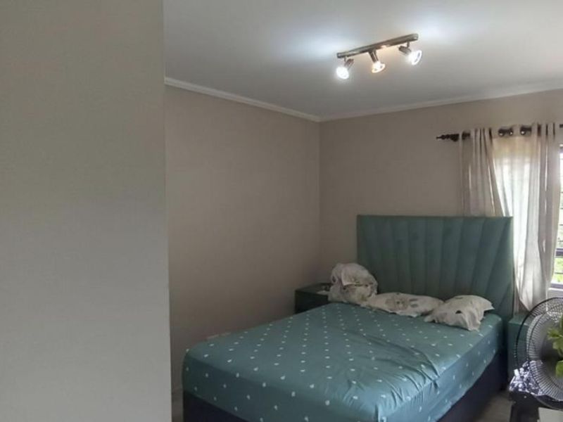 A functional bedroom featuring a ceiling-mounted spotlight fixture and a window fitted with security bars, providing natural light and ventilation.
