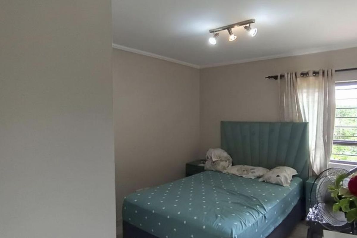 A functional bedroom featuring a ceiling-mounted spotlight fixture and a window fitted with security bars, providing natural light and ventilation.