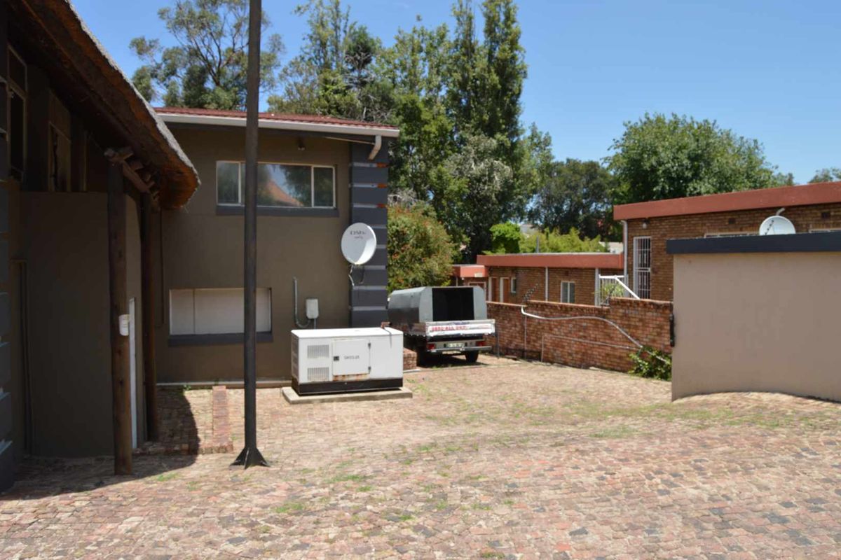 Rear exterior view of the property featuring a paved courtyard, brick boundary walls, and a fixed outdoor generator unit.