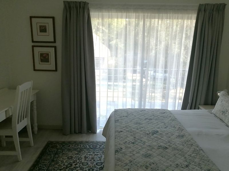 A bright bedroom featuring laminate flooring and a large sliding glass door with curtains, providing natural light and access to an outdoor area.