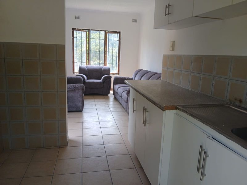 Open plan kitchen and living area featuring tiled flooring, built-in cabinetry with laminate countertops, and windows fitted with security bars.