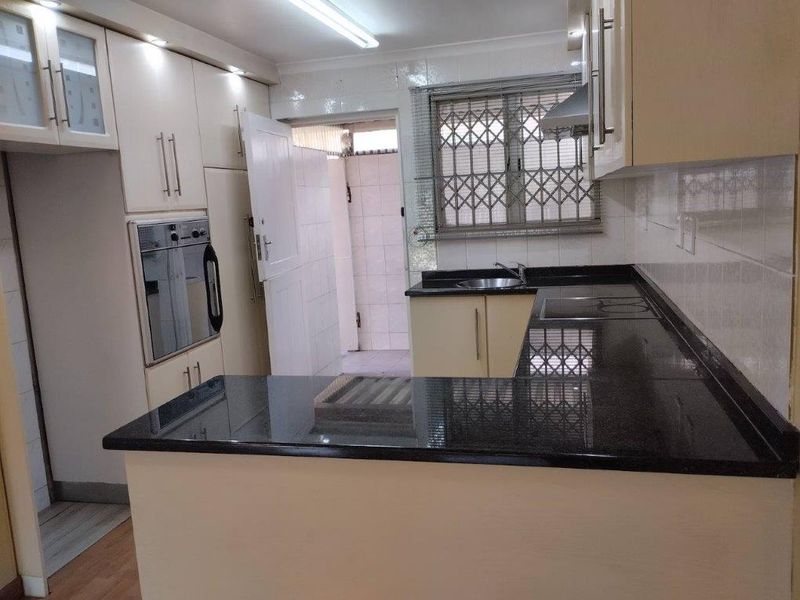 A functional kitchen featuring built-in cabinetry, granite countertops, a built-in oven, and an electric hob, with direct access to an exterior utility area.