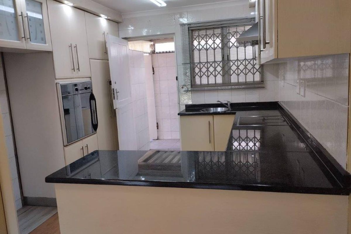 A functional kitchen featuring built-in cabinetry, granite countertops, a built-in oven, and an electric hob, with direct access to an exterior utility area.