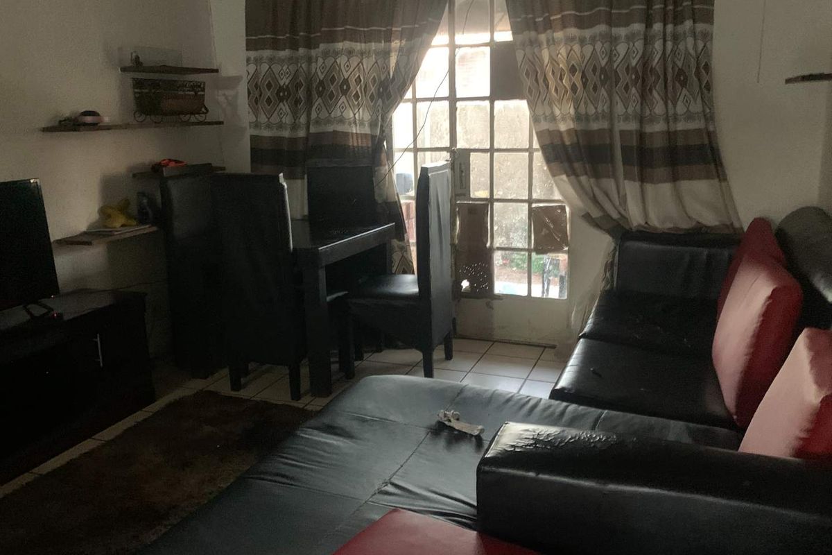 A living room area featuring tiled flooring and direct access to an outdoor space through a security gate and glass door.
