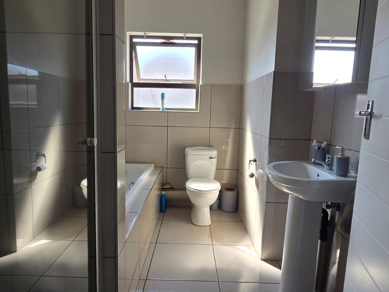A functional bathroom featuring a pedestal basin, a built-in bathtub, and a toilet, finished with neutral wall and floor tiling.