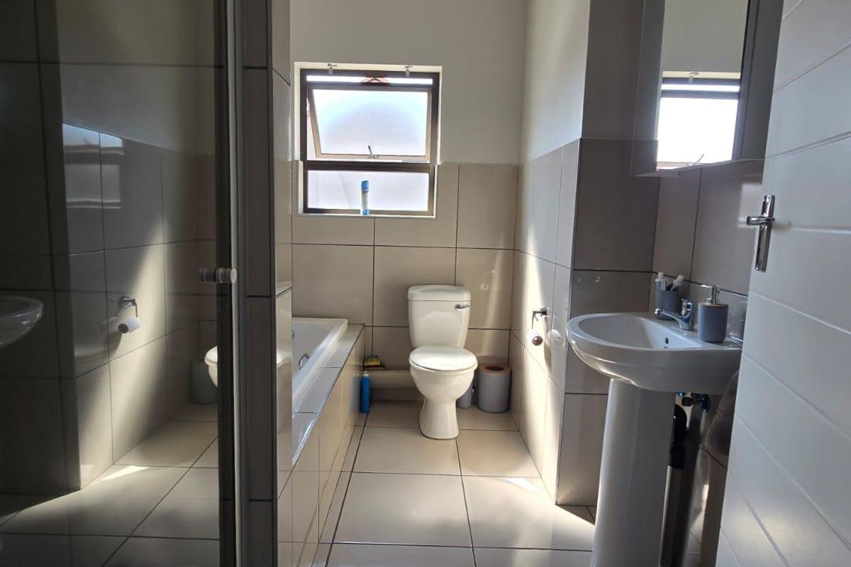 A functional bathroom featuring a pedestal basin, a built-in bathtub, and a toilet, finished with neutral wall and floor tiling.