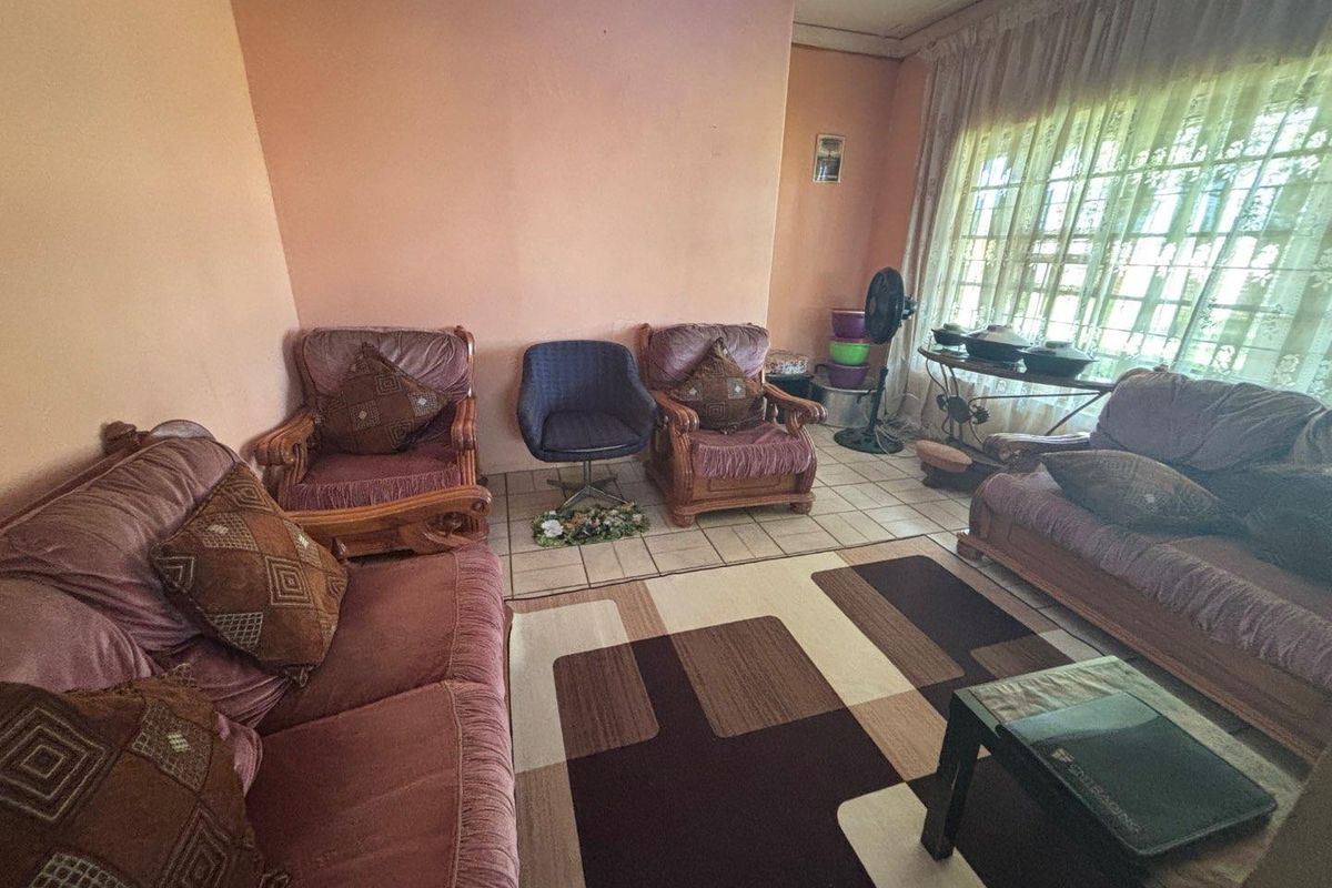 A dated living room featuring ceramic floor tiles, large windows with curtains, and plain wall finishes, offering a functional space for relaxation.