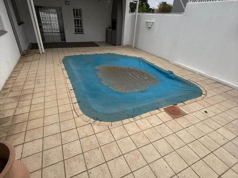 Outdoor pool area featuring a covered patio with a built-in braai, tiled flooring, and a perimeter wall with security spikes.