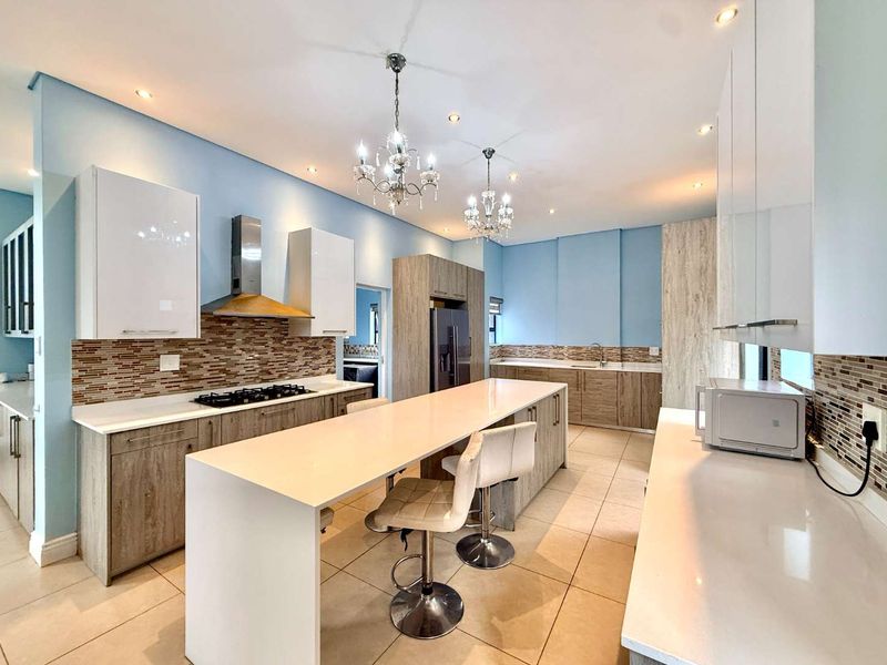 Modern kitchen featuring a large central island, stone countertops, gas hob with extractor, and ample built-in cabinetry with a stylish mosaic tile backsplash.