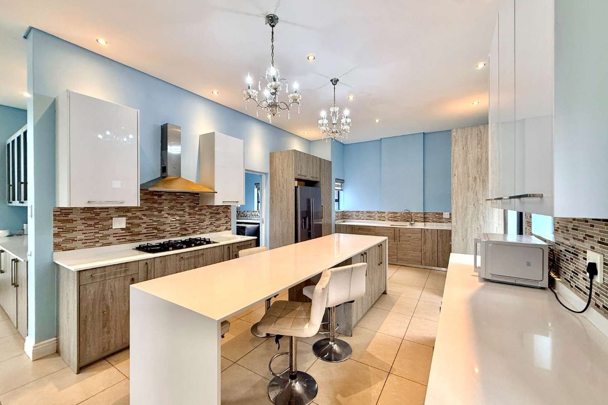 Modern kitchen featuring a large central island, stone countertops, gas hob with extractor, and ample built-in cabinetry with a stylish mosaic tile backsplash.